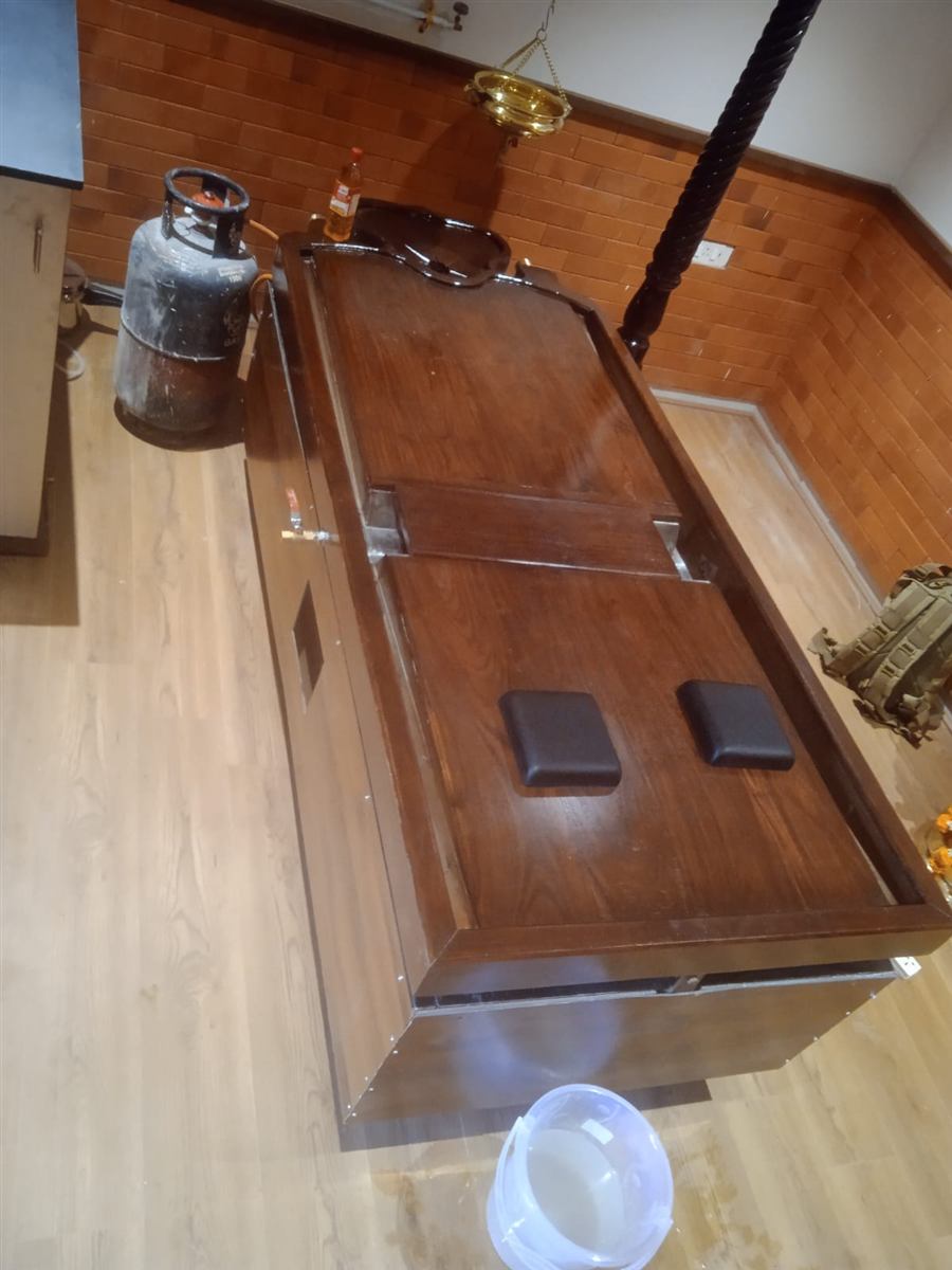 The Vedadhara Maha Droni, the flagship panchakarma table, mid-finish on the workshop floor with oil-channel and cushioned rests visible